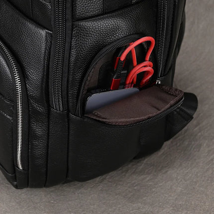 Close-up of the Black Leather Travel Backpack, showing a partially unzipped pocket with a smartphone and two red charging cables inside. The backpack is made of textured material with visible stitching, and offers a spacious interior along with multiple compartments secured by zippers.